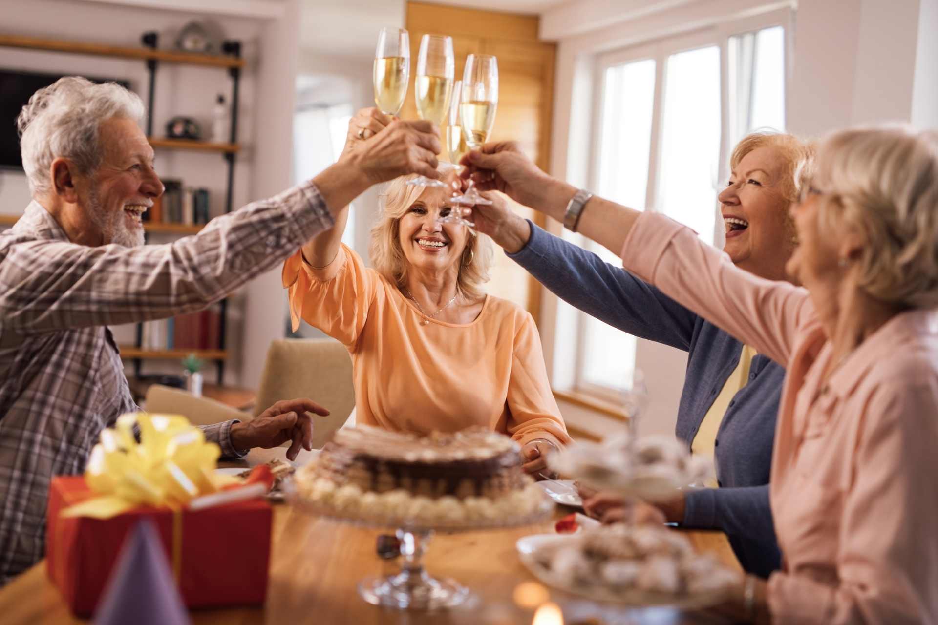 A group of senior friends toasting with glasses of champagne and enjoying cake together.